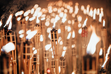 A captivating night scene of lit bamboo torches. Warm, flickering flames create a dramatic glow against the dark, with soft bokeh lights. Evokes ancient ritual, cultural celebration, and communal spir