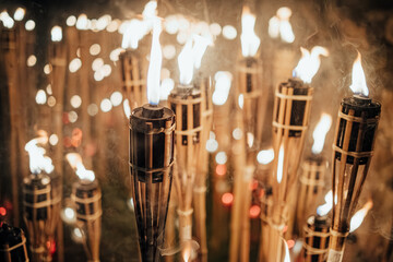 A captivating night scene of lit bamboo torches. Warm, flickering flames create a dramatic glow against the dark, with soft bokeh lights. Evokes ancient ritual, cultural celebration, and communal spir
