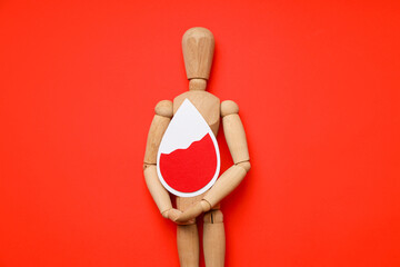 Wooden mannequin with a red drop on a red backdrop