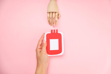 Hand holding a blood bag design against a pink background