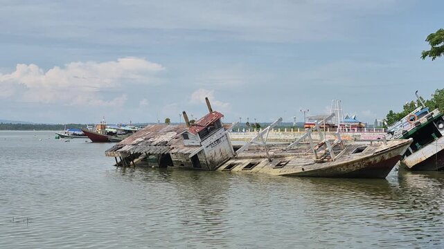 Abandoned wooden fishing boat shipwreck half submerged in shallow water in Kendari, Southeast Sulawesi, Indonesia
