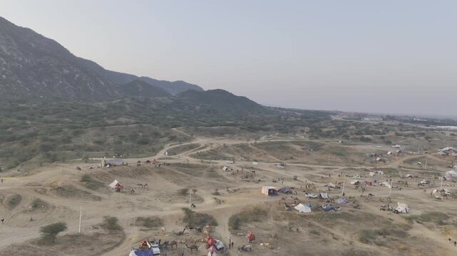 Shot of the Pushkar cattle fair ground showing camels and tents during the fair, with the Aravalli mountains in the background capturing the vibrant desert atmosphere.