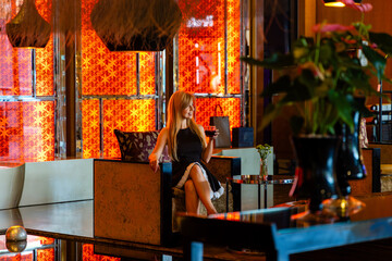 Woman relaxing with drink in luxury hotel lobby. Elegant setting with warm lighting, refined decor, and modern ambiance. Perfect for travel, lifestyle, and hospitality concepts.