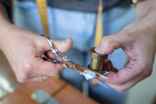 Hands cutting fabric with scissors and sewing bobbin - Powered by Adobe