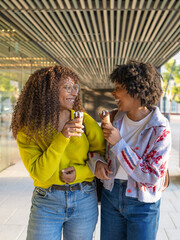 Two smiling women friends eating ice cream enjoying city walk