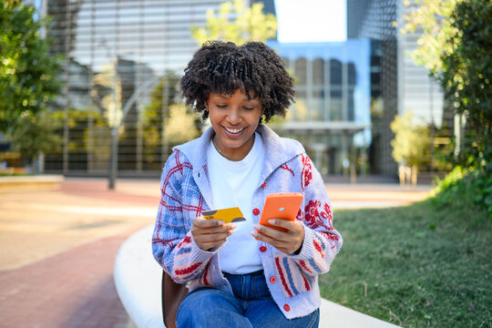 Young woman online shopping outdoors with credit card and phone