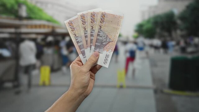 Man holds icelandic krona banknotes in an outdoor market setting, highlighting caucasian hand amidst a bustling street scene.