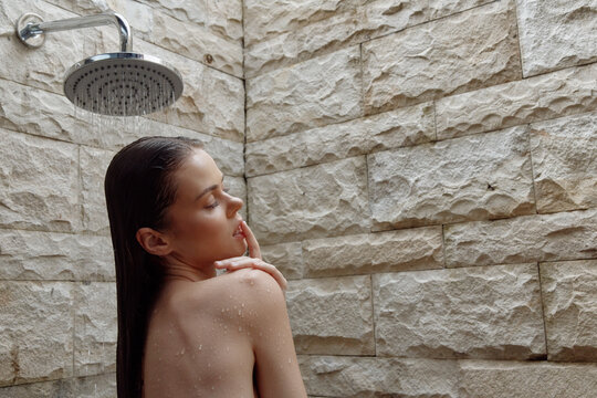 woman showering with wet hair under rainfall showerhead in stone bathroom, natural skin, relaxed mood, wellness and self-care moment - Powered by Adobe