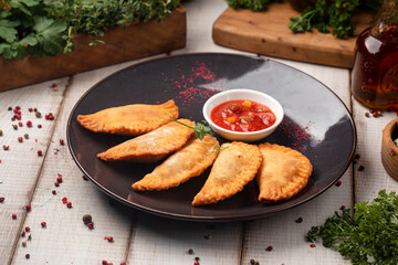 Golden crispy mini chebureki arranged on plate and served with rich spicy tomato dipping sauce