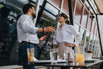 Two colleagues engage in a conversation at a cafe, surrounded by beverages and a relaxed outdoor atmosphere. The setting highlights a mix of collaboration and a casual work environment.