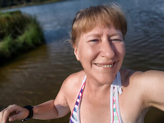 A cheerful blonde woman is soaking up the sun by the serene lake, eagerly snapping a joyful selfie