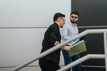 Casual business interaction of two coworkers walking outdoors while holding and referring to project folders