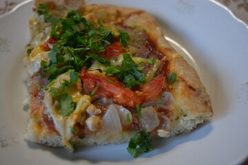 Food, groceries, homemade fresh baked goods. A large slice of pizza with chicken pieces, tomato slices, cheese, and fresh herbs sits on a ceramic plate.