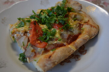 Food, groceries, homemade fresh baked goods. A large slice of pizza with chicken pieces, tomato slices, cheese, and fresh herbs sits on a ceramic plate.