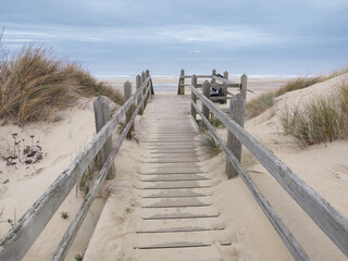 Wooden boardwalk leads to sandy beach under a cloudy sky in the afternoon