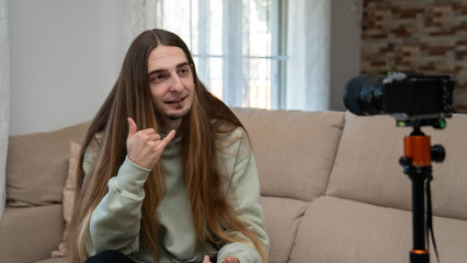 Young man vlogging at home, creating content and making shaka sign for online audience on a digital camera