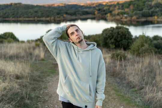 Young man with long hair relaxing on a path by a lake, expressing contemplation and connection with nature