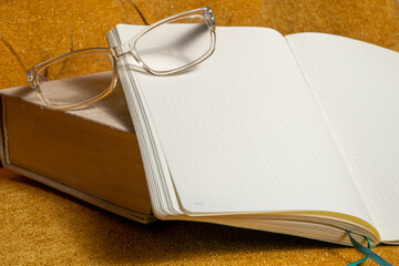 thick classic book, open blank notebook and a pair reading of glasses on mustard green sofa