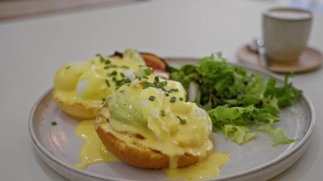 Delicious eggs benedict served on a plate with fresh greens and coffee in a cozy indoor restaurant setting.