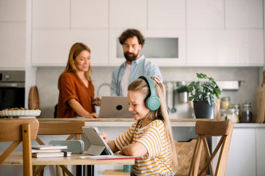 Child using digital tablet with headphones at home, parents in background