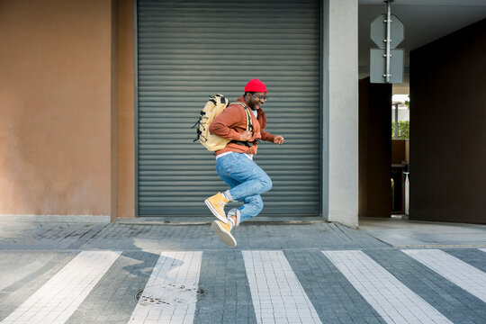 Cheerful man jumping on a street in casual clothes with backpack
