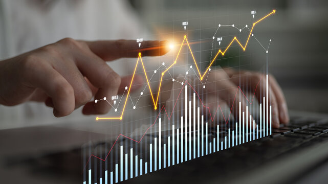 A business professional interacts with a glowing graph on a digital interface, showcasing analysis of data trends while working on a laptop in a modern office environment. Scalp