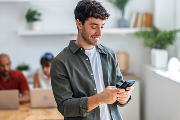Smiling businessman using mobile phone in modern office with team brainstorming