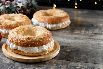 traditional Spanish Roscón de Reyes filled with whipped cream, decorated with sliced almonds and sugar on top on wooden table. Copy space