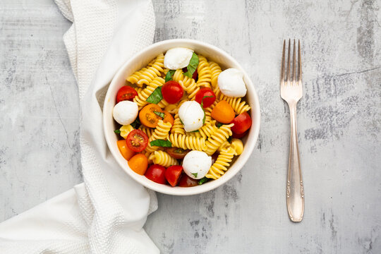 Fusilli pasta salad with mozzarella, tomatoes and basil on grey concrete