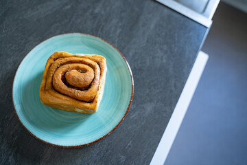 Classic cinnamon roll on an artisan ceramic plate in a home kitchen, top view. Warm tones and natural light create an inviting feel. Concept of breakfast, pastry, comfort, homemade.