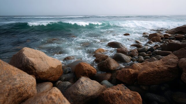 A rocky coastline with powerful waves crashing against boulders under an overcast sky