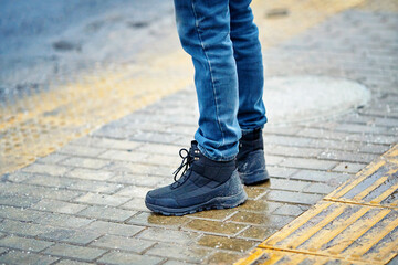 Closeup view of winter boots stands on wet pavement slabs before the pedestrian crossing where salt crystals are spread to melt ice, city safety measures during cold weather. Boots on salted walkway