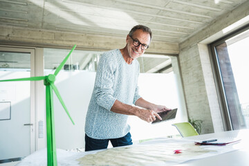 Happy man touching tablet PC screen and standing near wind turbine model at desk