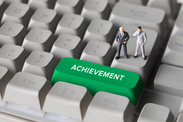 Miniature Business Figures Standing on Keyboard Button with Text Achievement. Symbolizing business success, goal accomplishment, performance improvement and motivation