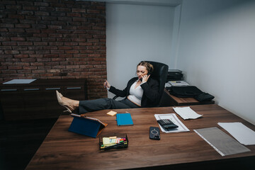 An energetic businesswoman multitasks in her office workspace, speaking on the phone while using...