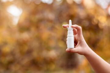 Allergy Nasal Spray Aerosol Bottle in Hand in Fall Autumn Background. Allergy Spray for Nasal Congestion and Runny Nose.