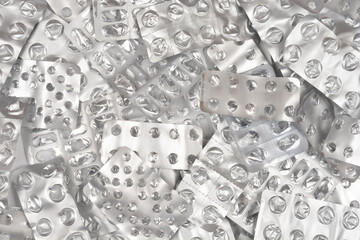 An abstract horizontal full-frame background of a large, overlapping pile of shiny, crumpled, and empty silver medicine blister packaging strips