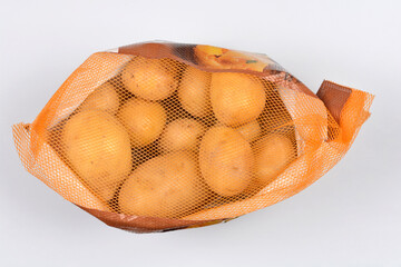 A studio shot shows a plastic mesh bag of small, round yellow potatoes placed diagonally against a clean, light gray background