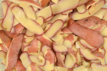 A close-up, full-frame photograph shows a pile of raw potato peelings with red skin and yellow flesh, creating an organic, overlapping texture
