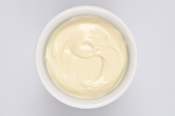 A creamy white chocolate pudding in a round plastic container is captured from a top-down view on a white background