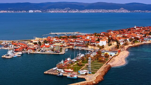 Coastal part of the city with dense red-roofed architecture. Sunny Nessebar, Bulgaria. Surrounded by the blue waterscape. Mountain range at backdrop.