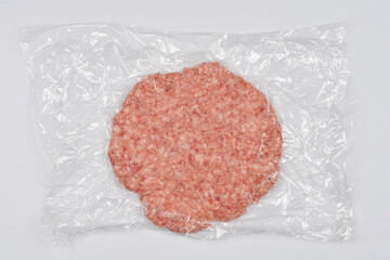 A raw ground pork patty is sealed in clear plastic wrap and displayed against a plain white background