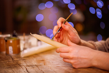 Hands of a creative individual painting a candle with vibrant colors, surrounded by art supplies and soft bokeh lights, showcasing the artistic process and craftsmanship
