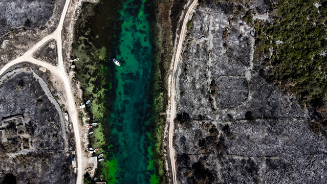 Aerial view of emerald waters cutting through scorched earth, contrasting starkly with the remnants of boats along the shore, Zaton, Zadar County, Croatia.