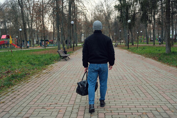 Man walking alone on park path carrying black bag