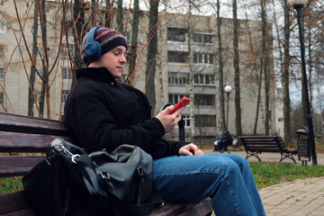 Young man relaxing on park bench using smartphone and listening to music with headphones