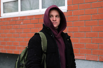 Young man in hoodie backpack standing by brick wall