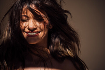 Smiling woman with flowing hair illuminated by soft light, showcasing joyful expression and natural beauty in a serene environment, capturing the essence of happiness and warmth