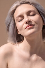 Young woman with light hair, eyes closed, enjoying sunlight on her face, showcasing natural beauty and tranquility in a serene atmosphere, emphasizing relaxation and self-care