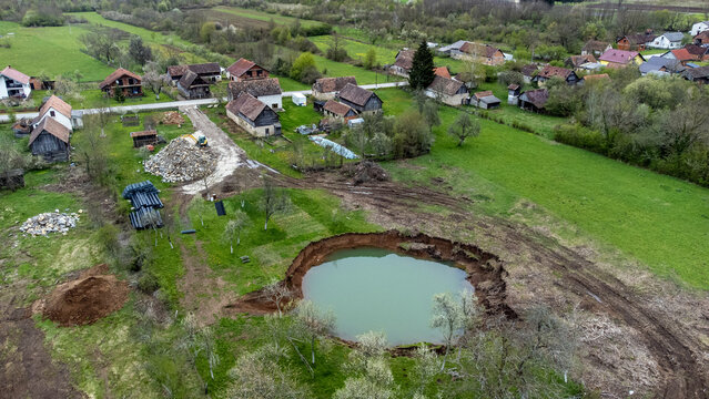 Aerial view of a collapsed sinkhole filled with water amid a rural landscape with scattered houses, Petrinja, Sisak-Moslavina County, Croatia.